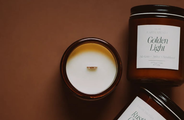 Flat lay of luxury scented candles with wooden wicks in amber glass jars on a warm brown background