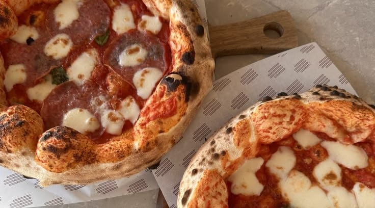 Two wood-fired pizzas with melted cheese and pepperoni on parchment paper